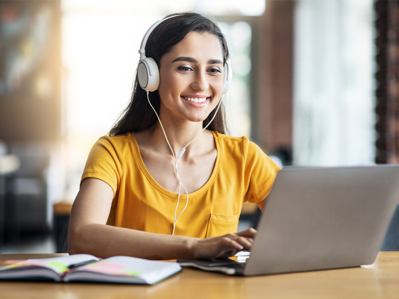 Mulher jovem com fones de ouvido digitando em um notebook e sorrindo