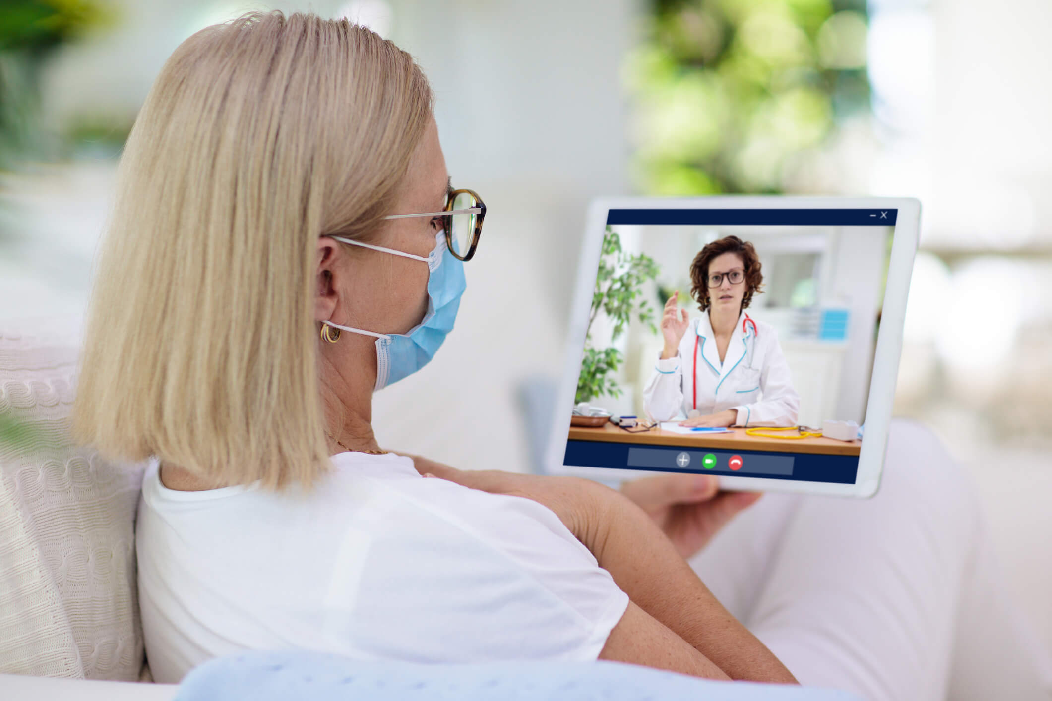 Imagem de mulher fazendo o uso da máscara e sendo atendida por médica em tele consulta por meio de seu tablet.
