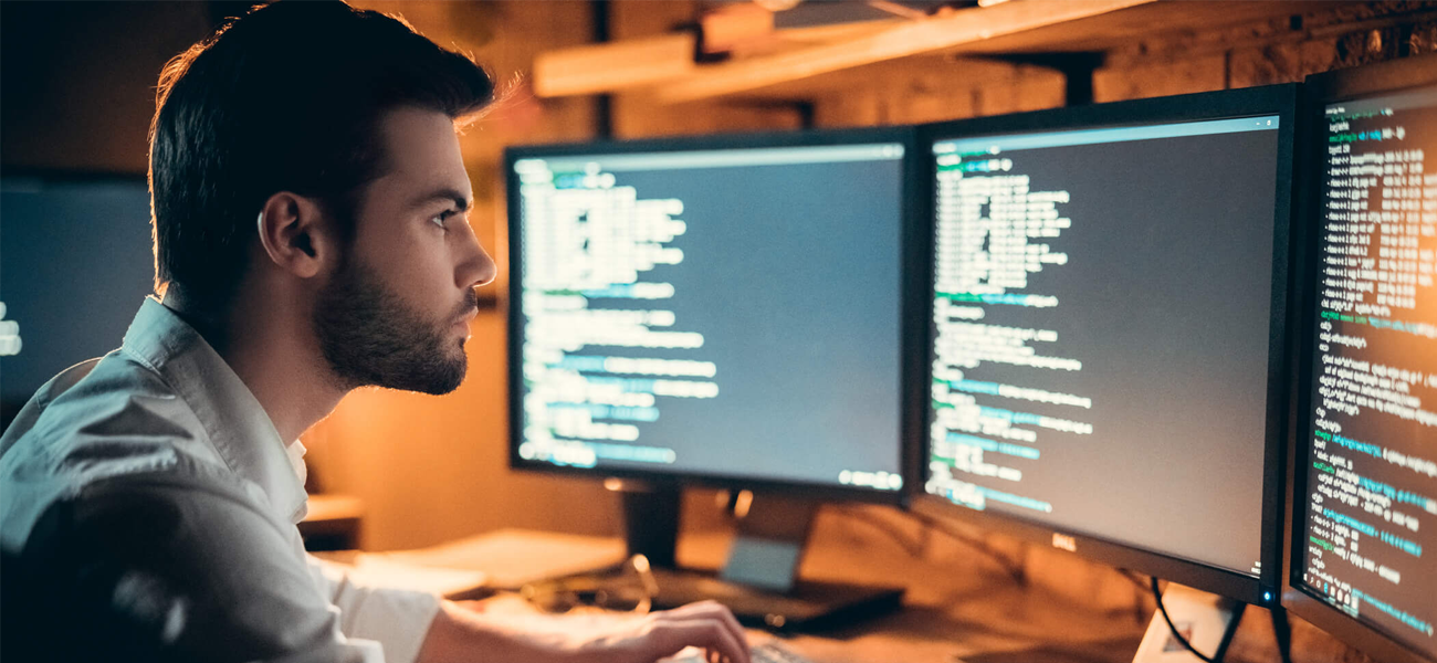 Home jovem olhando para 2 telas de computador exibindo código-fonte